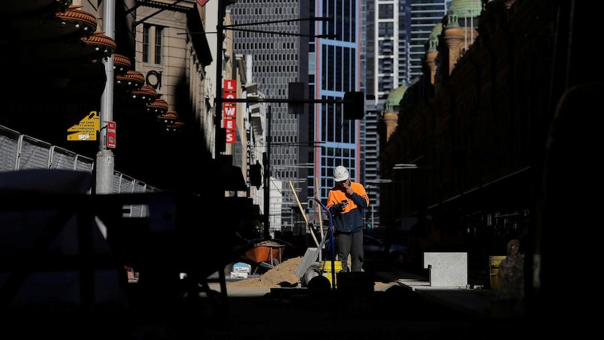 A construction worker smokes a cigarette as he looks at his mobile phone on a worksite in Sydney, Australia