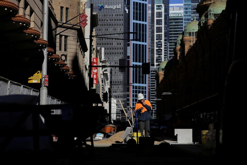 A construction worker smokes a cigarette as he looks at his mobile phone on a worksite in Sydney, Australia