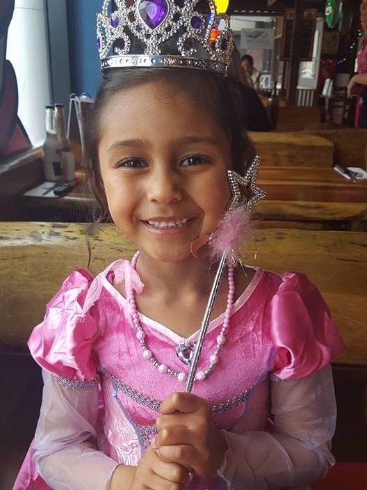 A little girl in a fairy dress holds a wand at a restaurant.