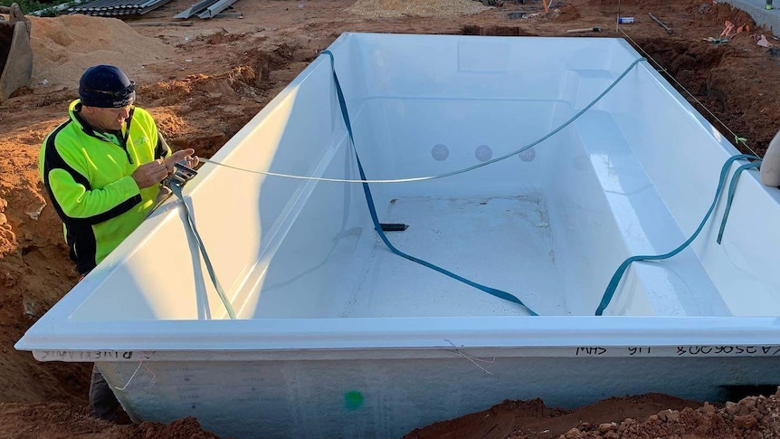 An empty pool sits unfinished in a purpose built hole while construction work happens around it to get it ready for use