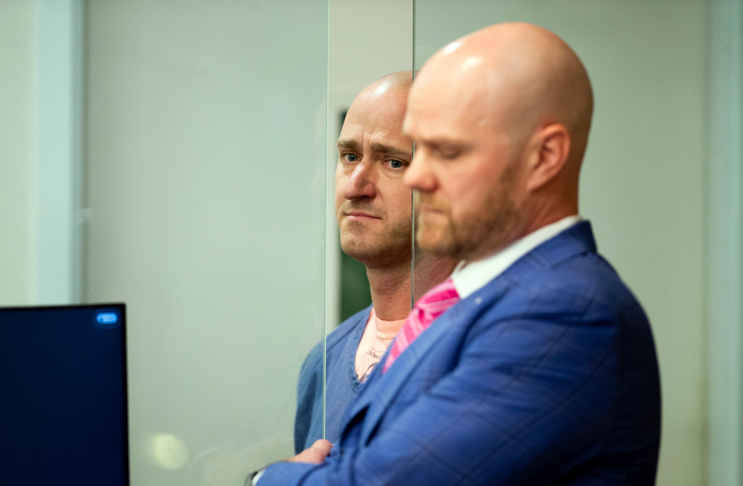 Joseph David Emerson standing behind protective glass in court as another man in a suit stands to the side of him