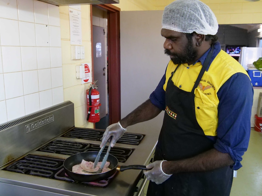 A young Indigenous man cooking bacon at a stove.