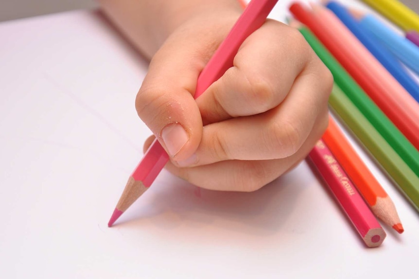The hand of a young child who is drawing with a pink pencil.