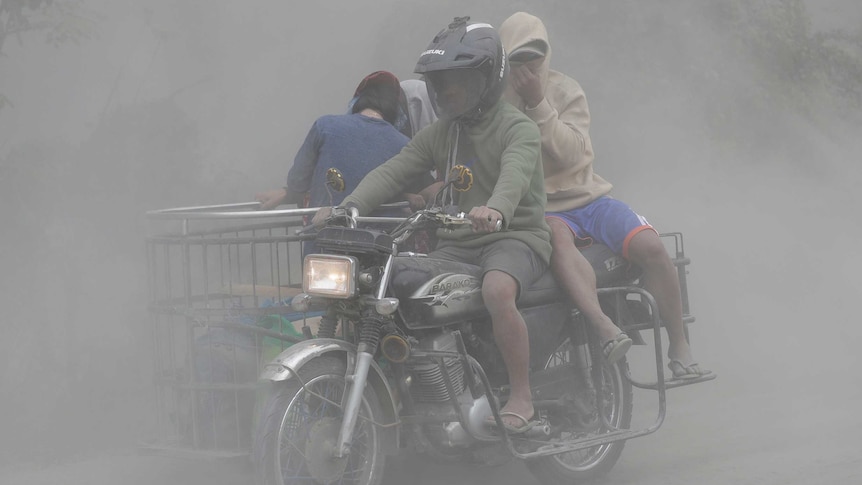 A family rides their motorcycle through clouds of ash as they evacuate to safer grounds.