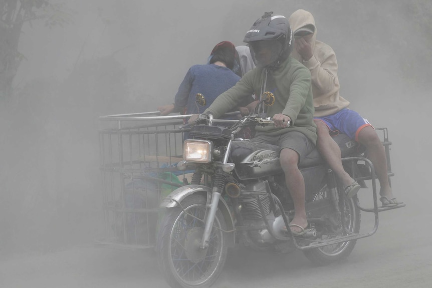 A family rides their motorcycle through clouds of ash as they evacuate to safer grounds.