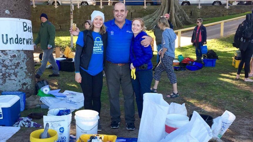 Three people standing behind a pile of recovered plastic rubbish.