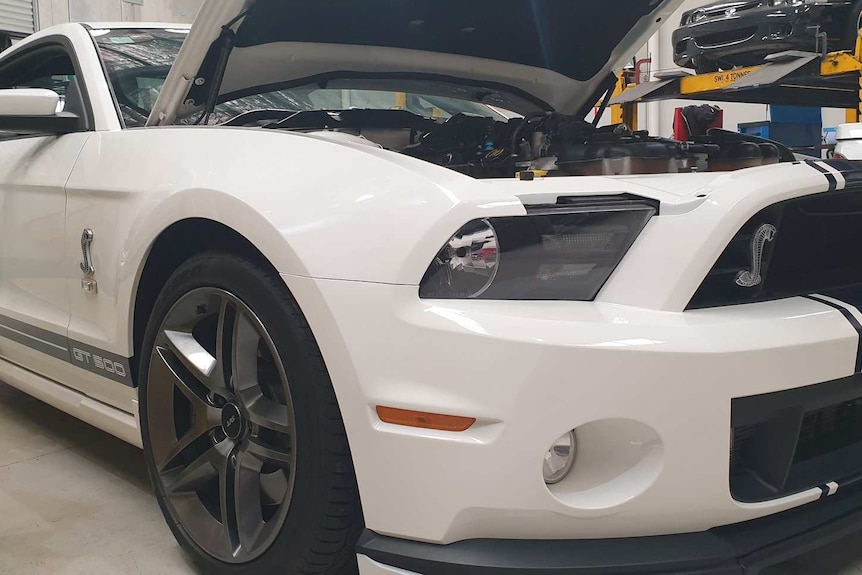 A white hotted up Mustang car in a garage with its bonnet open.