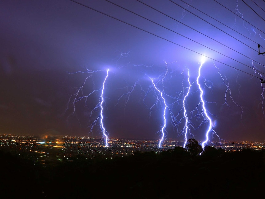 Four forks of lightning strike a city at night.