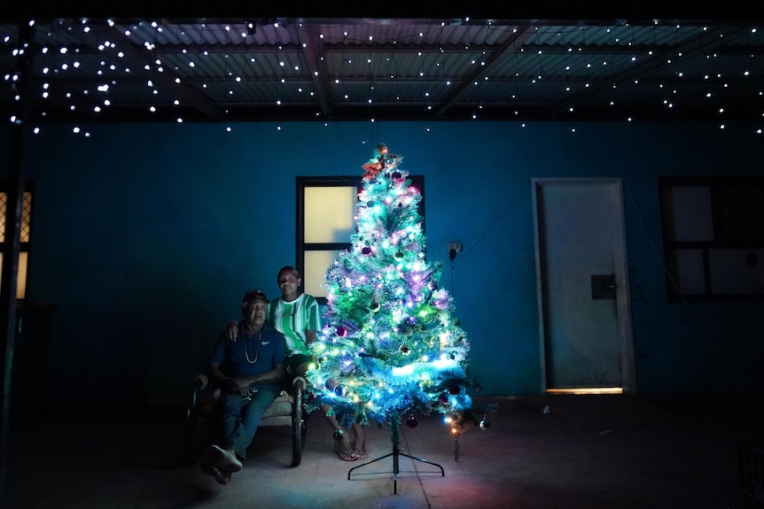 Two people sit beside their christmas tree