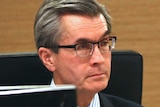 A head and shoulders shot of Tony Power wearing a suit and tie sitting in an inquiry.