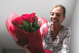 A smiling woman being given a bunch of red roses in a stairwell for a story about staying connected amid coronavirus