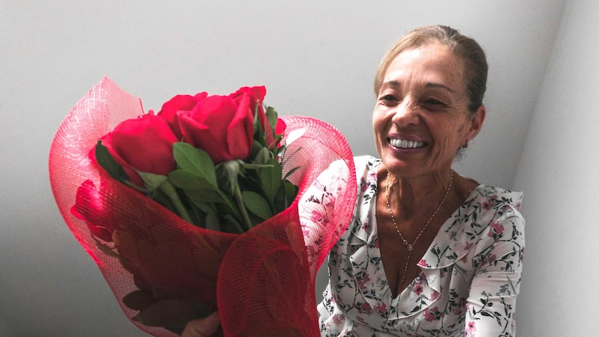 A smiling woman being given a bunch of red roses in a stairwell for a story about staying connected amid coronavirus
