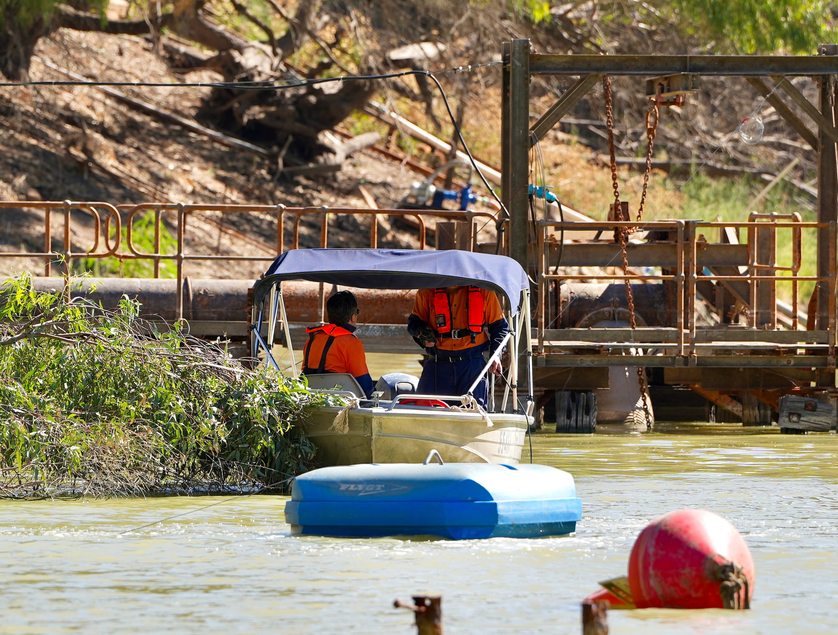 Two men wearing orange shirts and lifejackets test the water along the Darling River at Menindee. 