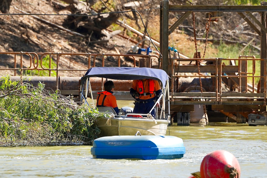 Two men wearing orange shirts and lifejackets test the water along the Darling River at Menindee. 