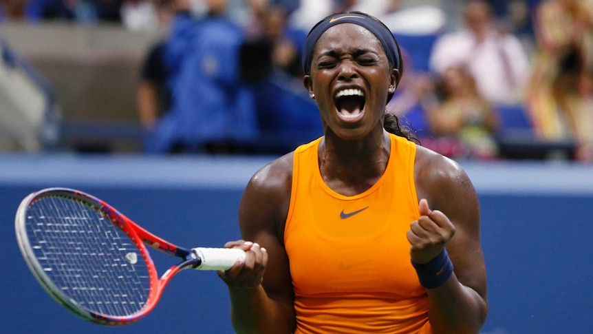 A female tennis player wearing bright orange clenches her fists, closes her eyes and screams