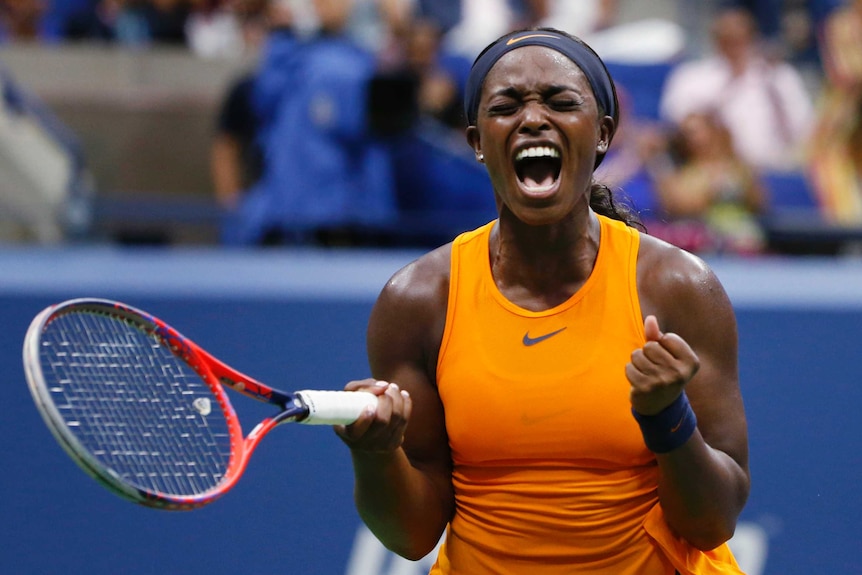 A female tennis player wearing bright orange clenches her fists, closes her eyes and screams