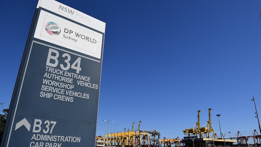A sign that says DP world at a dock with cranes in the background. 