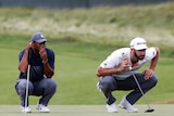 Tiger Woods and Duston Johnson crouch down and look ahead of them on the green.