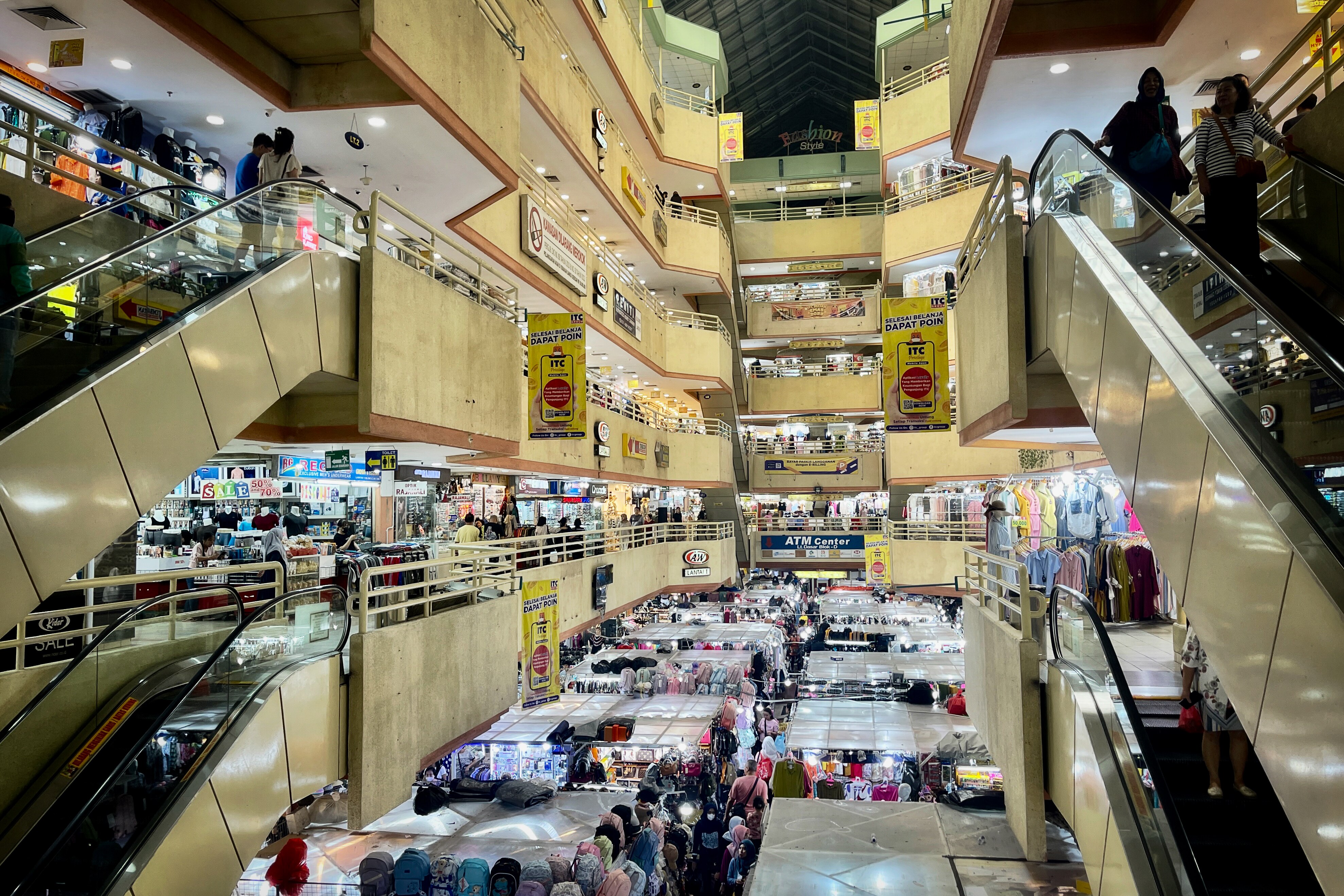 A set of escalators is seen inside an open shopping centre with stalls on the ground floor