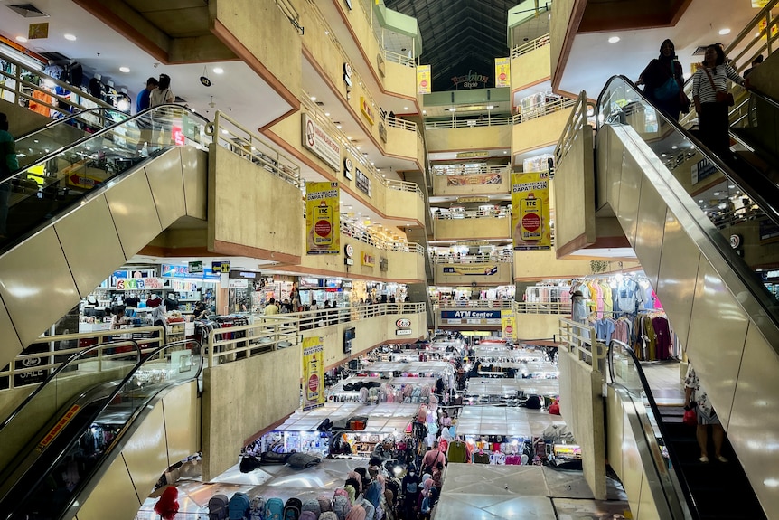 A set of escalators is seen inside an open shopping centre with stalls on the ground floor