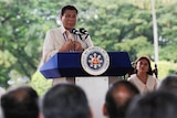 Rodrigo Duterte stands behind a large blue lectern carrying the Filipino presidential seal in front of greenery.