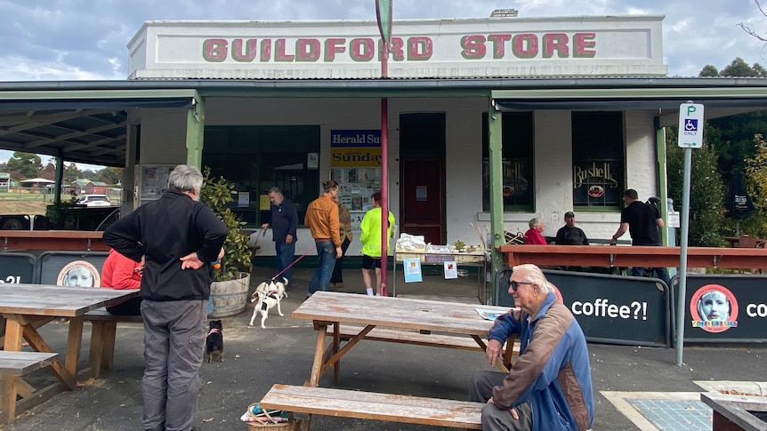 A group of people sit outsdie the general store talking and drinking coffee