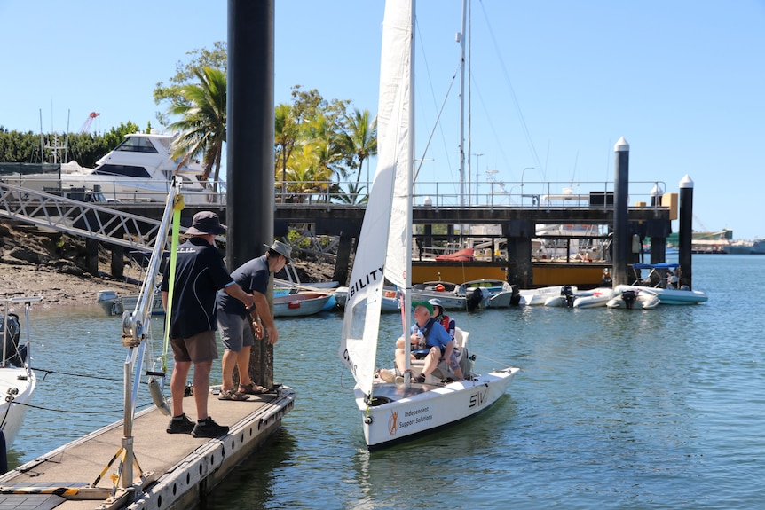 two men helping a sailboat coming back to the pier