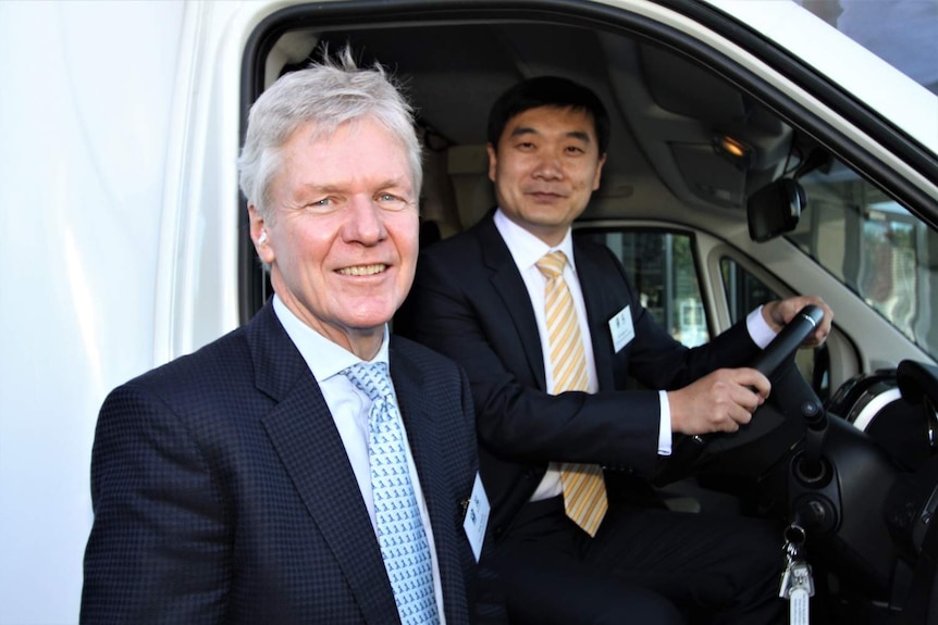Tony Smith (left) stands next to Lou Weijian (right) who sits in drivers seat over campervan