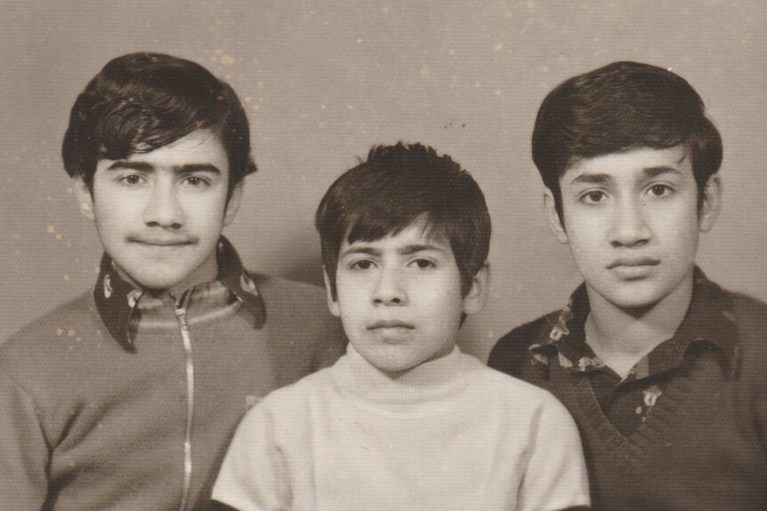Three boys sit next to each other looking at the camera in a black and white image.