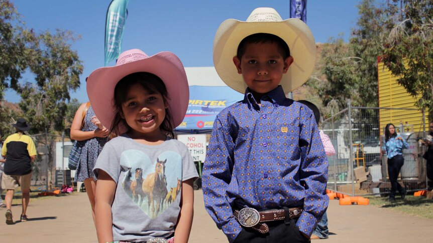 Young siblings standing beside each other in cowboy hats.