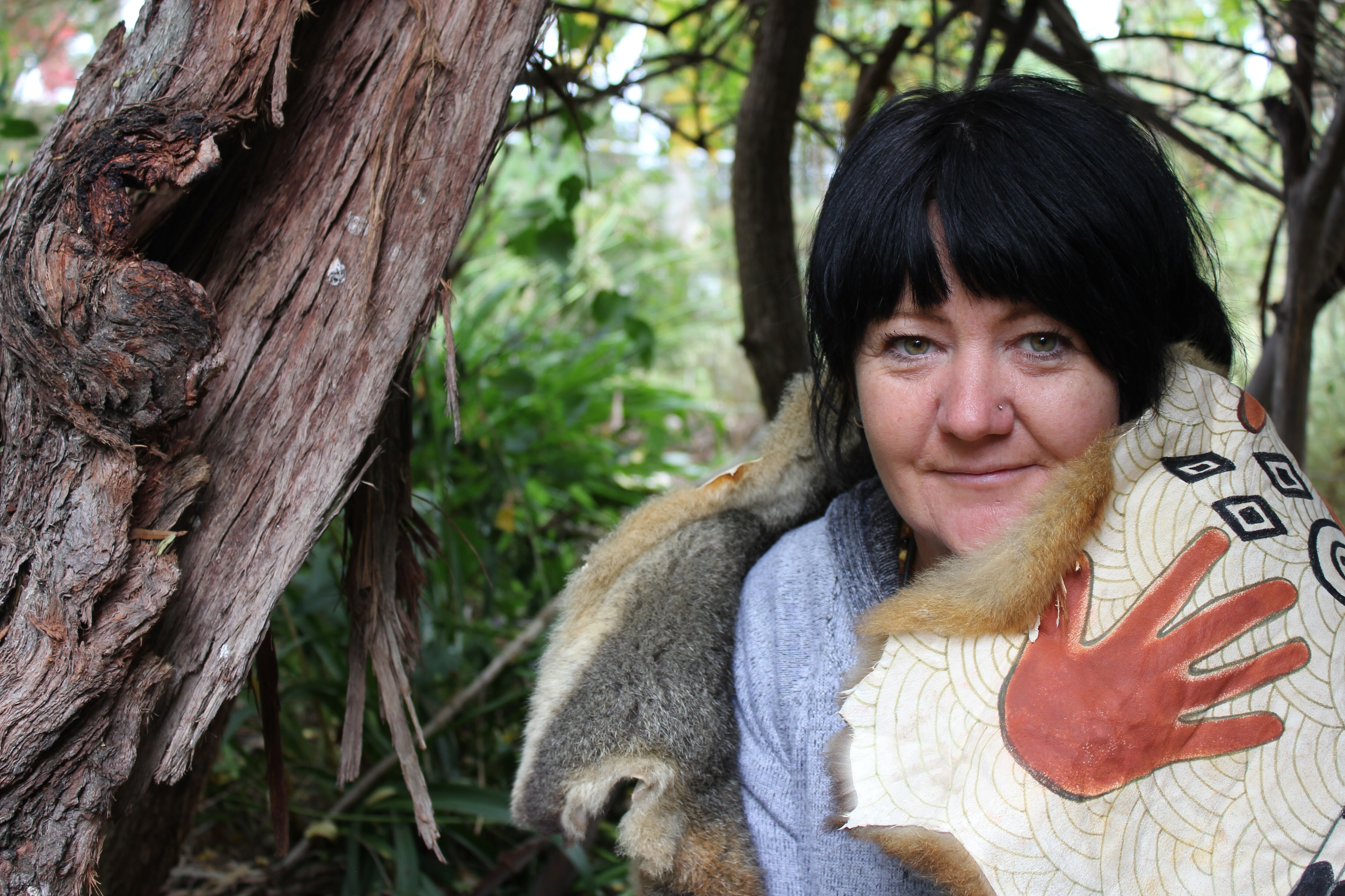 Aboriginal artist Cassie Leatham sits under a tree with an animal skin over her shoulder