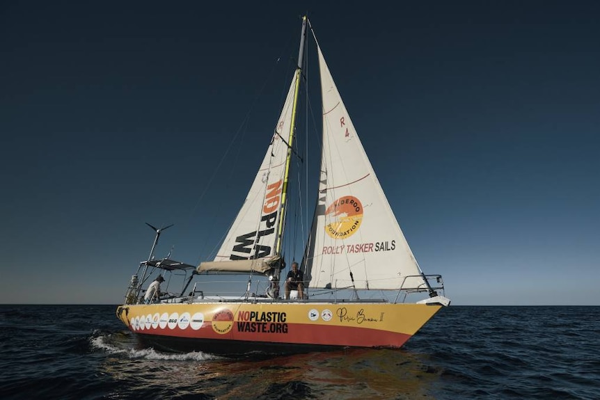 Yach with "no plastic waste" written on hull and sails in the middle of a blue ocean and deep blue sky.