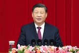 Close up of Xi Jinping seated with microphones and flowers in front of him.