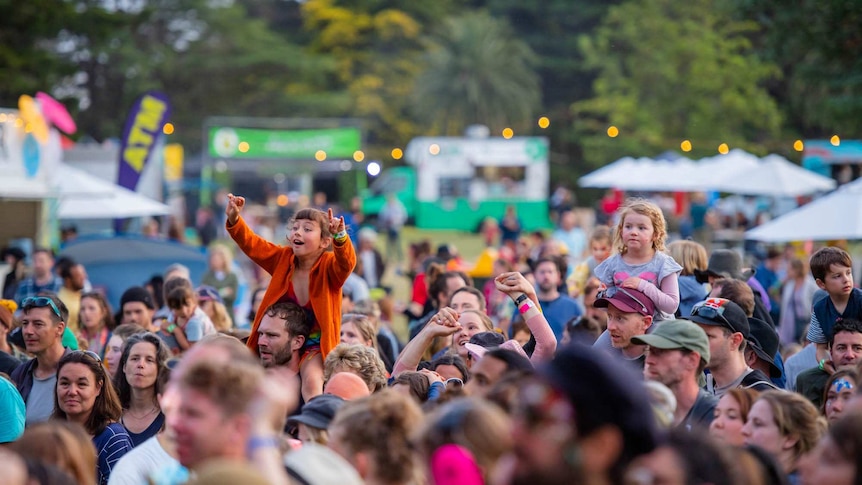 Children sit on the shoulders of their parents in a crowd of people watching a band at Lost Lands Festival