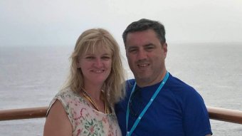 A woman and a man wit their arms around each other stand at a rail.