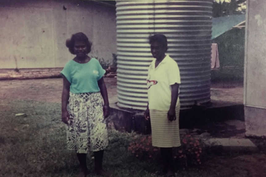 Old, faded photograph of two women standing outside old building in Papua New Guinea.
