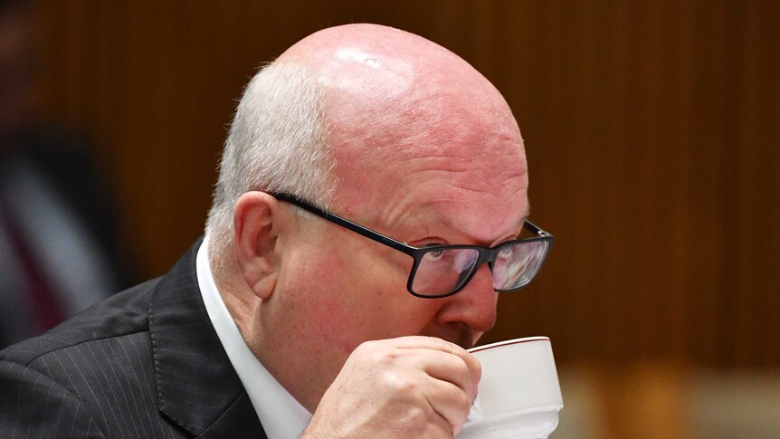 Attorney-General George Brandis drinks from a cup at senate estimates