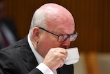 Attorney-General George Brandis drinks from a cup at senate estimates