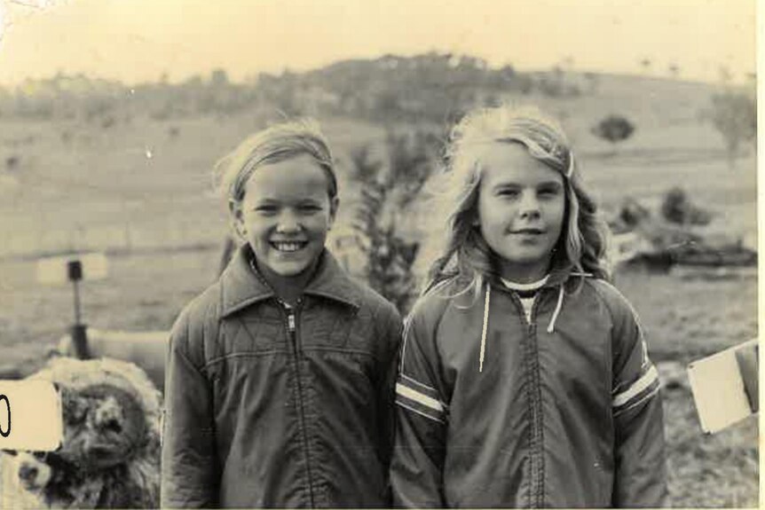 Black and white mid shot of two young girls in a rural setting.