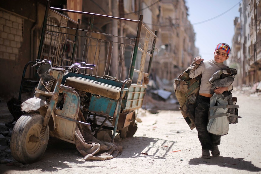 Boy walks along damaged street in Douma
