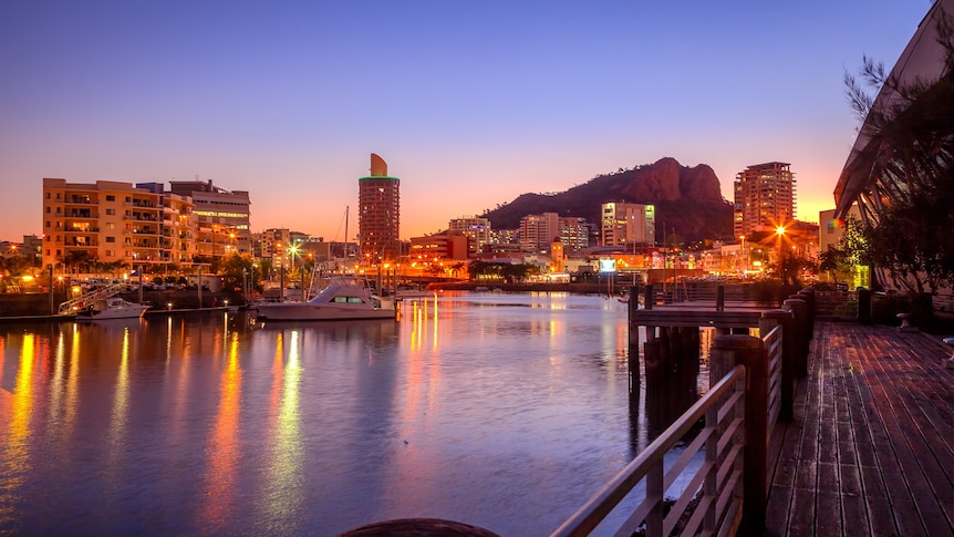 View across an enclosed body of water at sunset, with buildings and boats of Townsville's maria on the opposite side. 