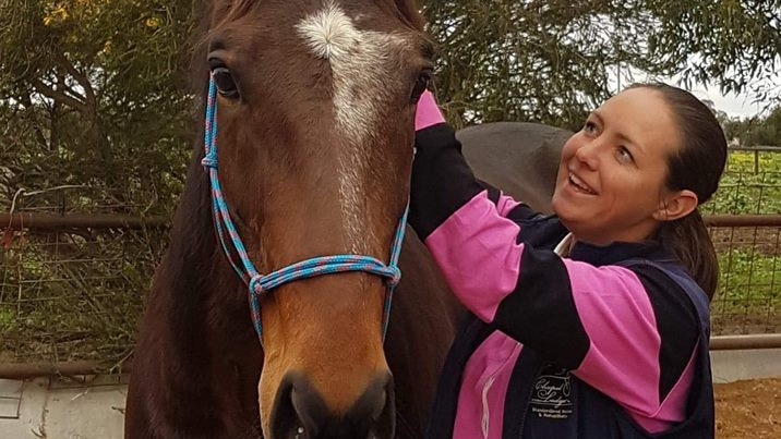 Kerry Rose stands and smiles beside one of her rescue standardbred racehorses.