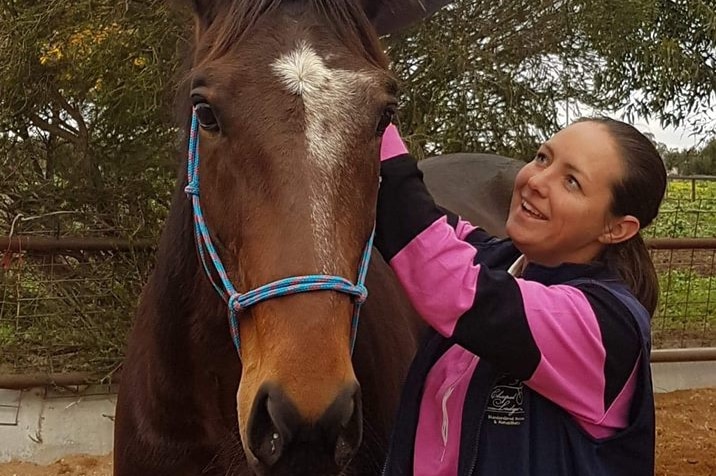 Kerry Rose stands and smiles beside one of her rescue standardbred racehorses.