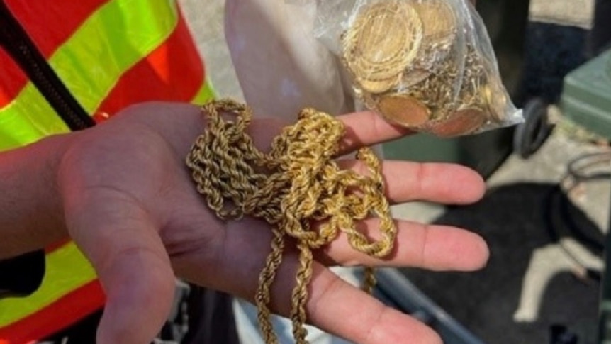 A person in a high-visibility vest holds a bag of gold jewellery.