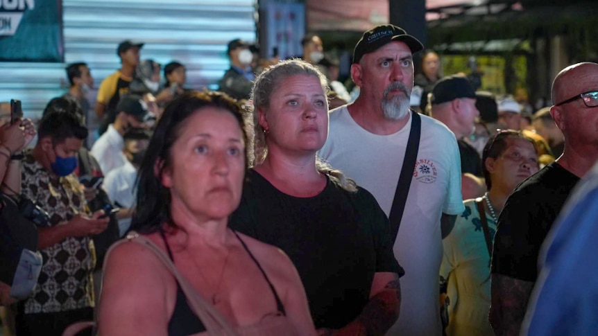 Two women and a man looking sternly in a crowded outdoor space 