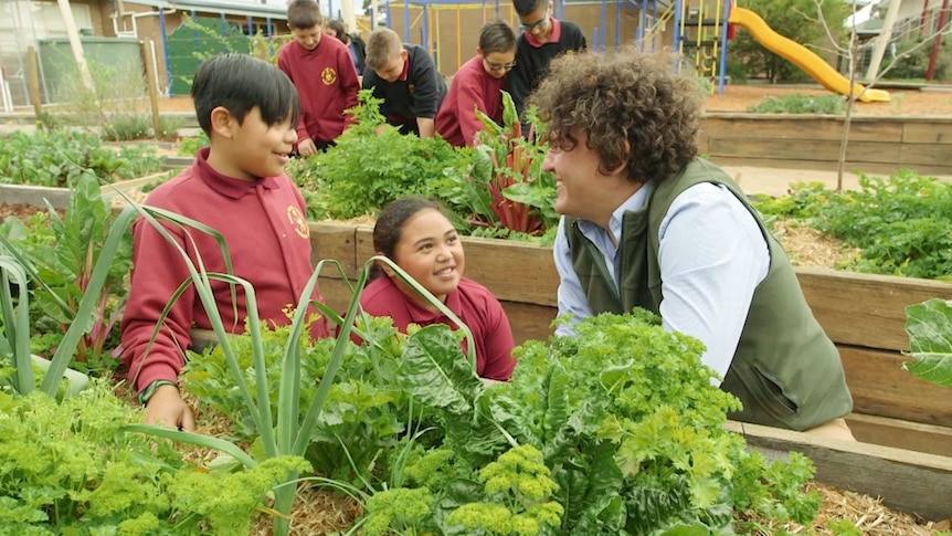Two school children and presenter sitting amongst vegie beds filled with edible plants
