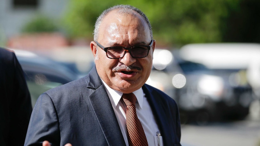 Papua New Guinea Prime Minister Peter O'Neill is pictured in a navy suit as he waves to the camera.