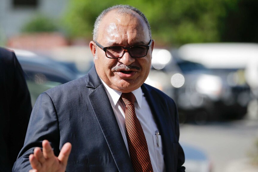 Former Papua New Guinea prime minister Peter O'Neill is pictured in a navy suit as he waves to the camera.