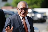 Former Papua New Guinea prime minister Peter O'Neill is pictured in a navy suit as he waves to the camera.