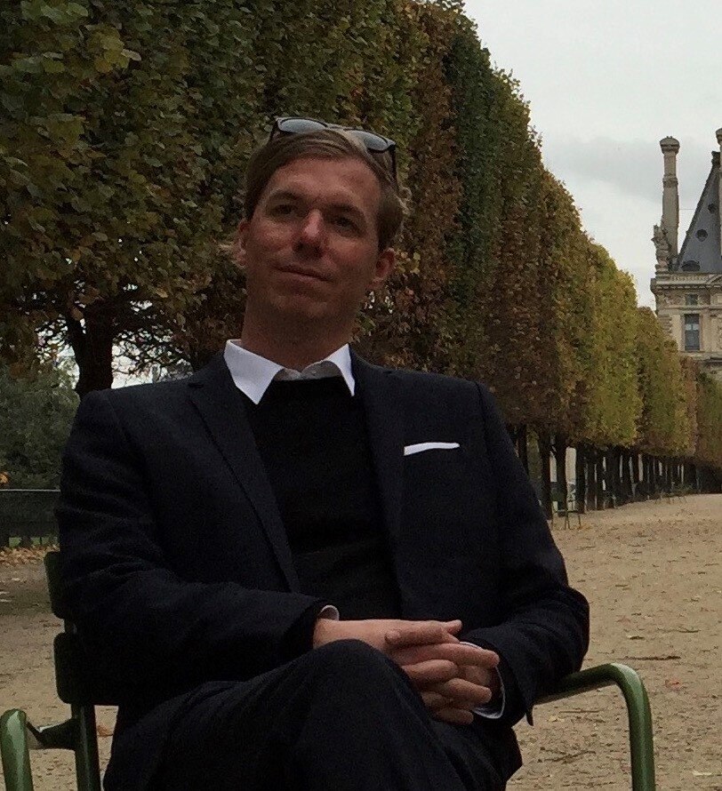 A man wearing a black suit sitting outside at a university.